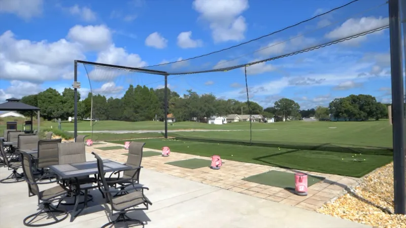 Practice range at golf club with tables and seating areas.