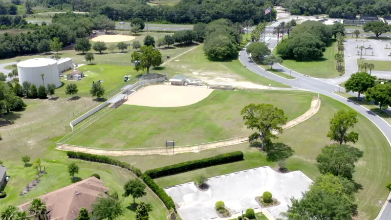 Community softball court with green grass and large trees scattered around.