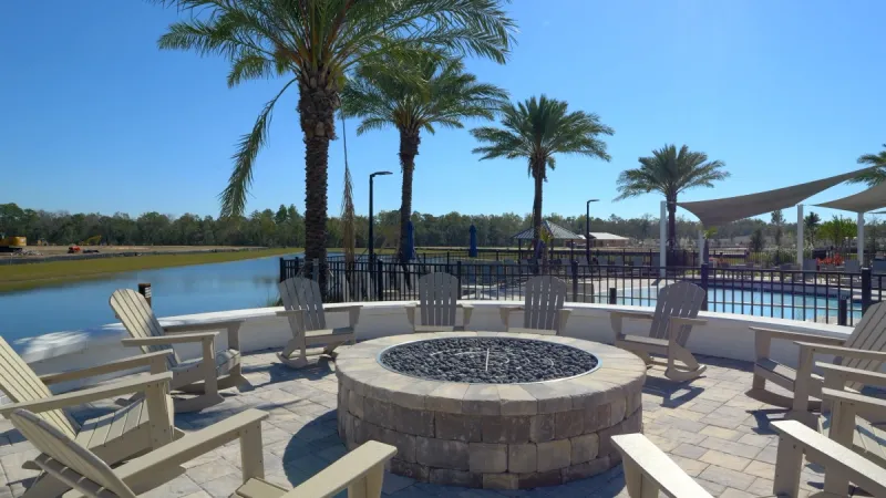 A community firepit surrounded by Adirondack chairs, overlooking a lake with large palm trees in the background at WaterSong at RiverTown.