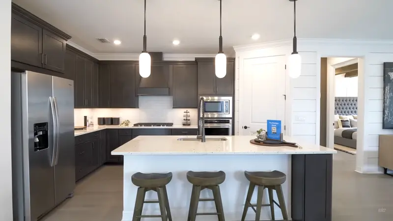 A modern kitchen with dark cabinetry, stainless steel appliances, a white island with bar stools.