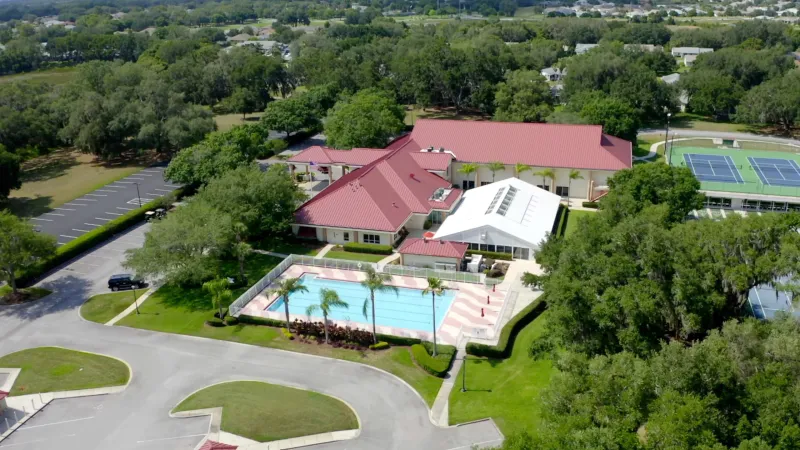 Highland Lakes clubhouse, pool, and sports courts surrounded by trees.