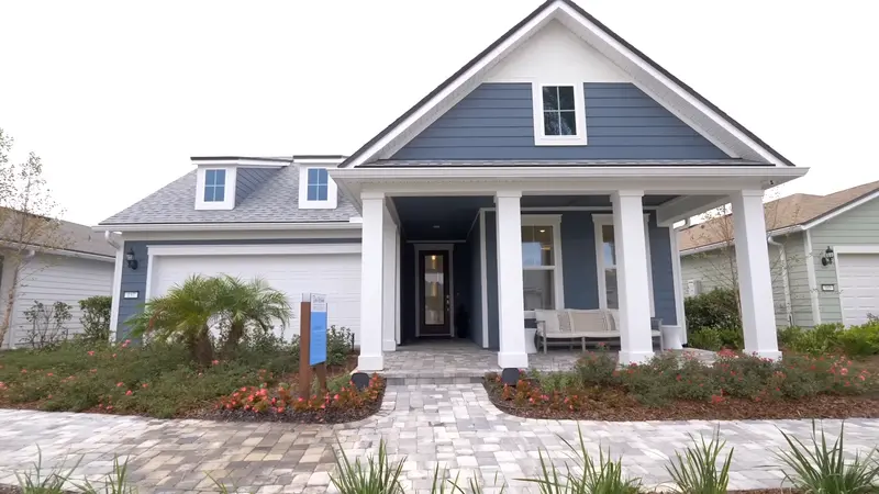 A blue and white house with a welcoming front porch and landscaped path in the Del Webb Wildlight community.