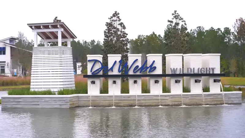 A lakeside entrance sign for Del Webb Wildlight, featuring modern white columns and a water feature.