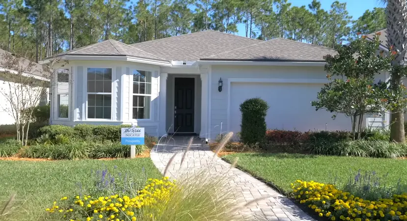 An exterior view of a Del Webb Nocatee home with white and grey tones, a well-manicured lawn, and a welcoming path leading to the front door.