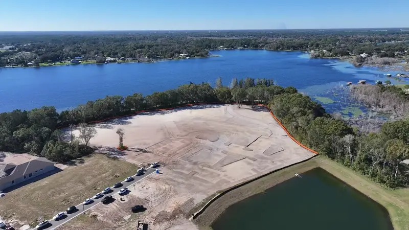 Aerial view of a large cleared construction site at Cresswind DeLand near a body of water with a surrounding residential area in the background.