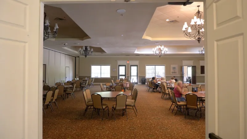 A community ballroom with elegant chandeliers and round tables set for gatherings.