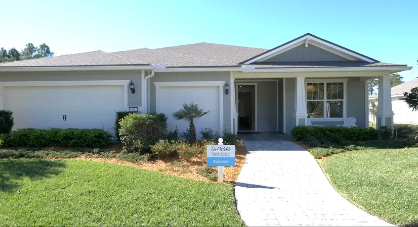 The front view of a charming Del Webb Nocatee home featuring a shaded porch area, light blue siding, and lush landscaping.
