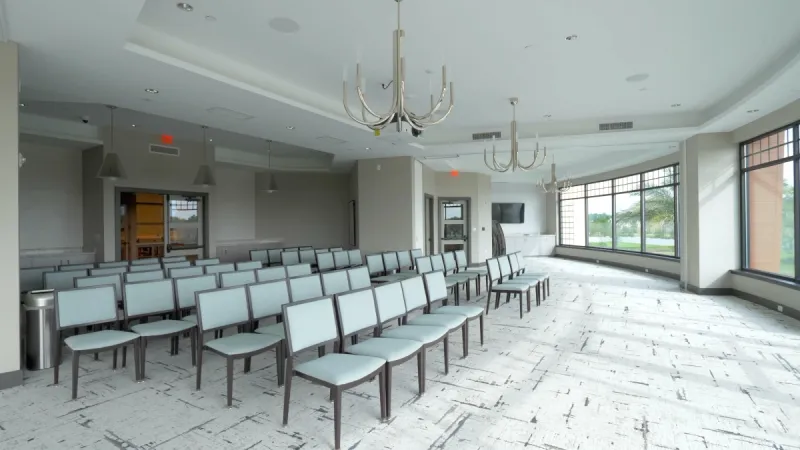 A Del Webb eTown meeting room featuring rows of chairs, contemporary chandeliers, and large windows allowing natural light.