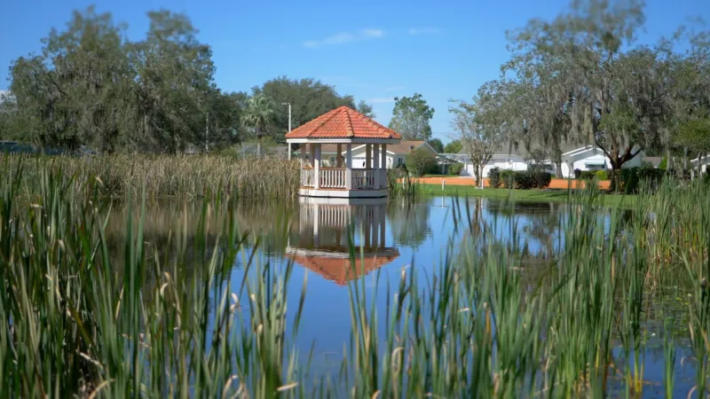 A gazebo at Spruce Creek South overlooking a pond surrounded by tall reeds, with a backdrop of trees and homes.