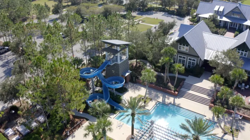 A clubhouse with a childrens pool area and exciting water slide, nestled amidst towering trees.