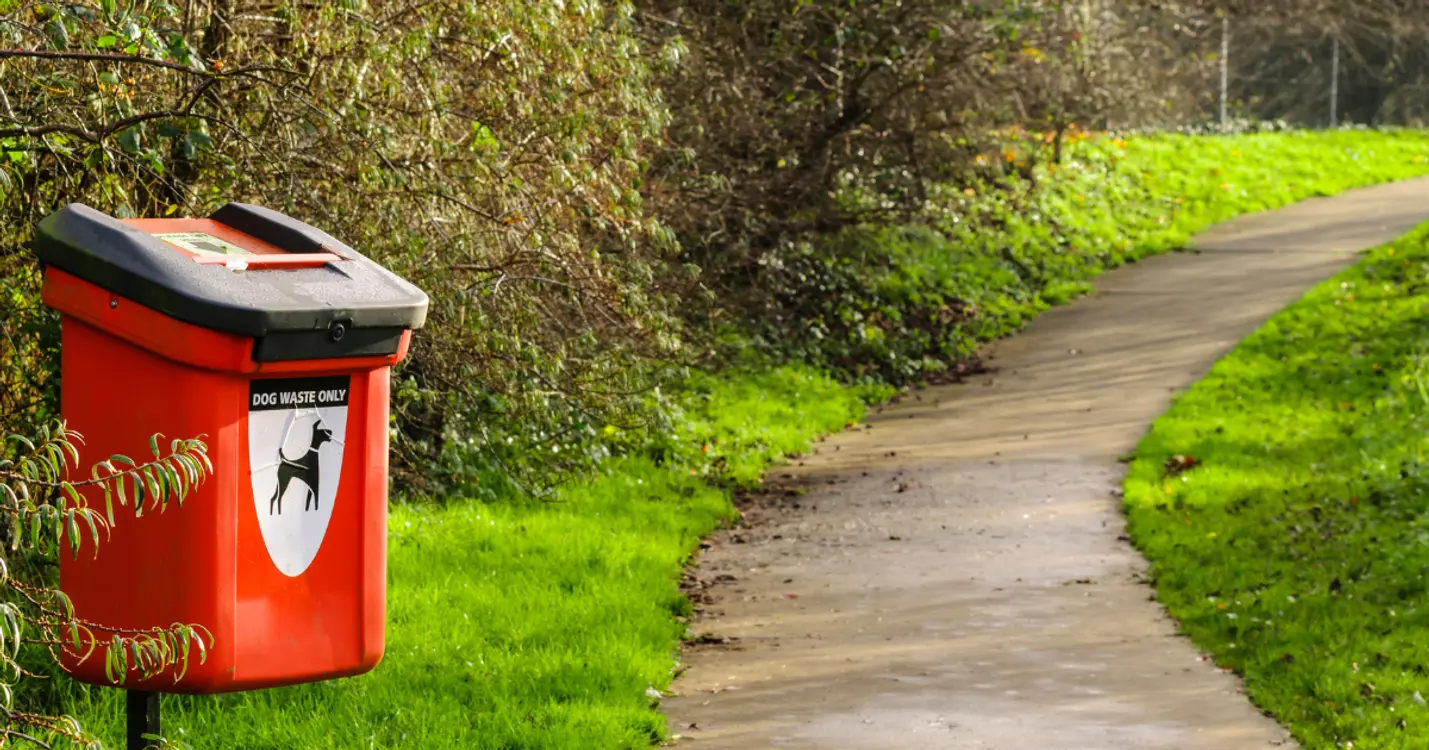 Dog waste bin along a walking trail in a pet-friendly 55+ community park.