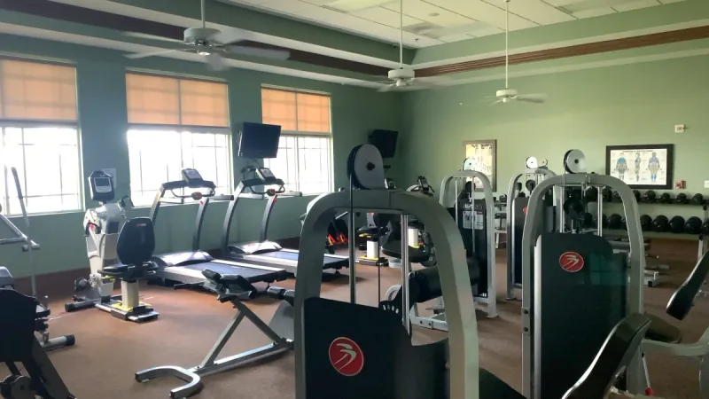 A well-equipped weight room, filled with a variety of resistance and weight training equipment, including weights, cardio equipment, and strength training machines.