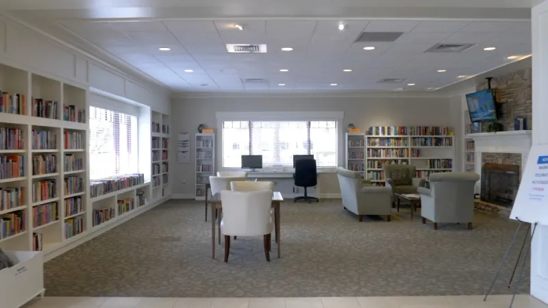 Community library with book-lined shelves, computers, and cozy seating areas near a fireplace.