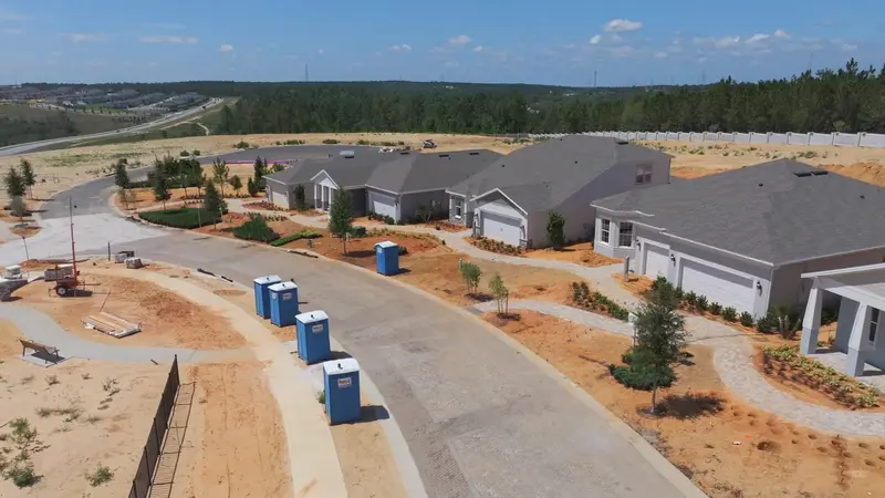 An aerial shot of a street within Del Webb Minneola, where several new homes with gray rooftops are surrounded by freshly planted trees and sandy lots ready for landscaping.