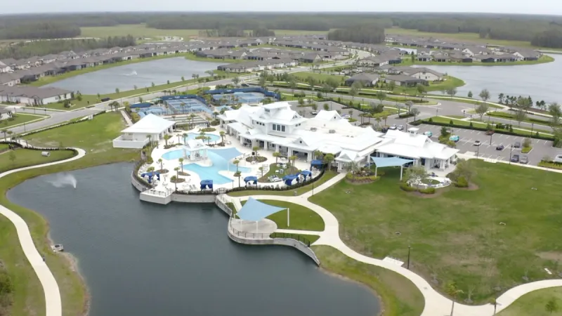 A clubhouse and community amenities nestled alongside a serene lake, with homes and additional lakes in the backdrop.