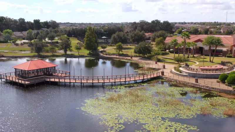 Aerial view of a screened-in gazebo and dock leading to the clubhouse and firepit area. Sports courts and homes can be seen in the background.