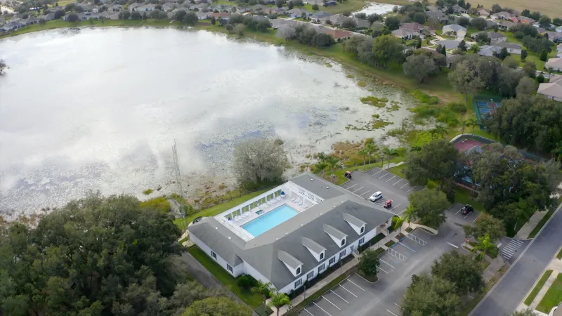 A stately clubhouse with a glistening pool in the back, and a picturesque lake visible in the distance behind it.