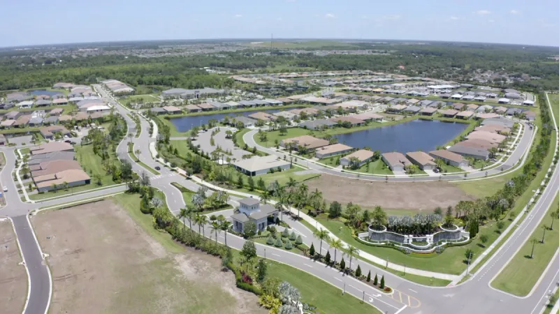 An aerial view showcases a pristine community with tree-lined streets, collections of homes and sparkling water features.