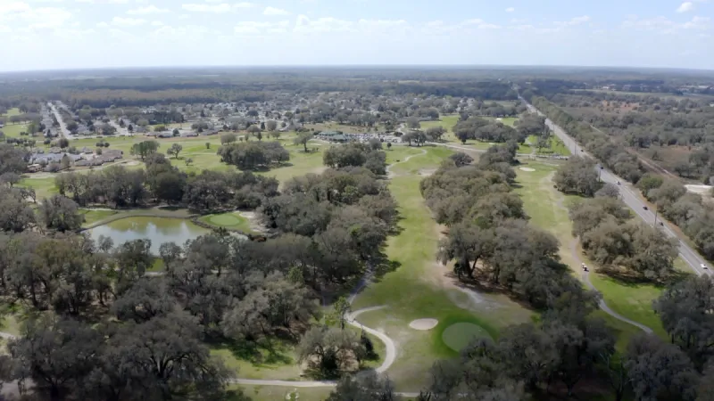 Sprawling tree lined golf course with pond and homes in background.