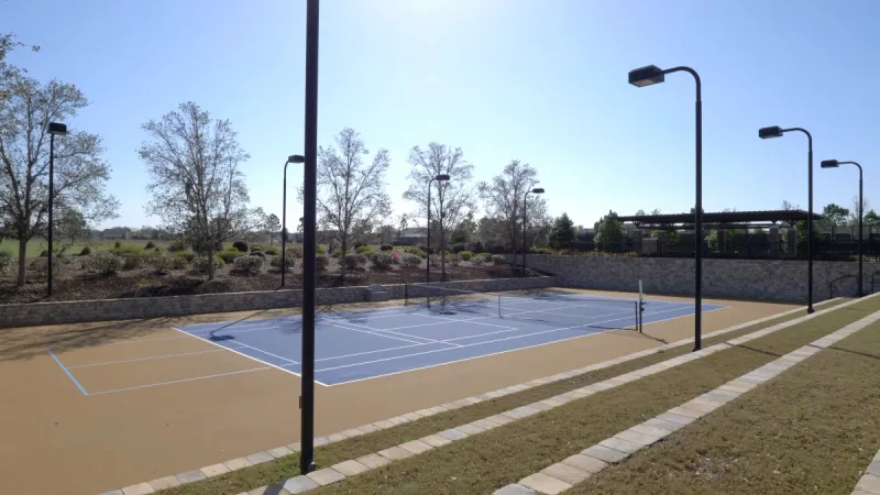 Tennis court surrounded by landscaping and lighting. 