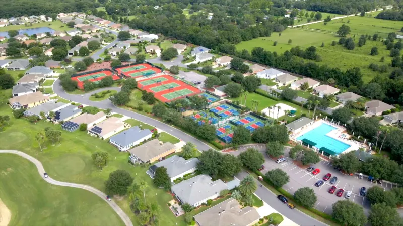 Aerial view capturing the layout of neighborhood homes, integrated with community amenities including a sparkling pool, pickleball courts, and tennis courts.