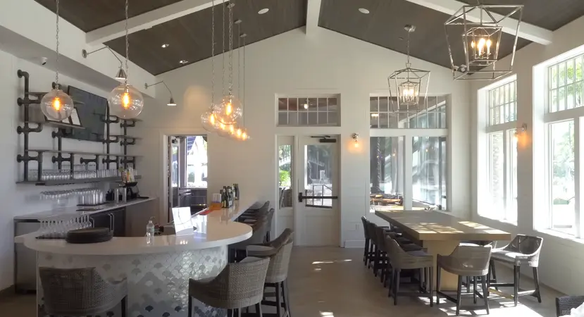 A bright and airy cafe interior with modern hanging lights and a bar setup, offering a comfortable dining space at Del Webb Nocatee.