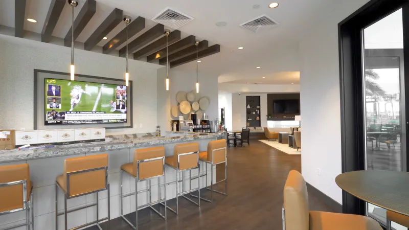 Spacious community bar area with modern stools, pendant lighting, and a large TV screen, adjacent to a cozy lounge space.