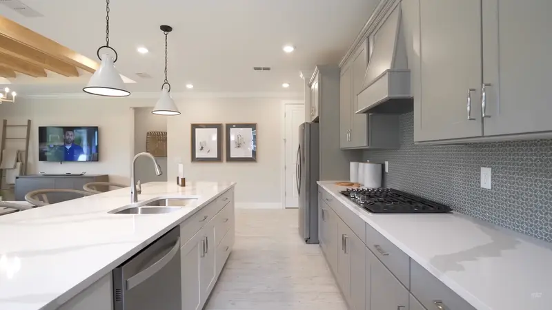 A spacious kitchen with white countertops, gray cabinetry, and two hanging pendant lights over the island.
