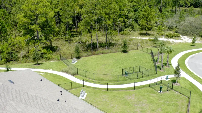 Fenced dog park surrounded by trees and walkways.