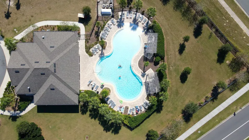 Crystal clear pool behind community clubhouse surrounded by green landscaping.