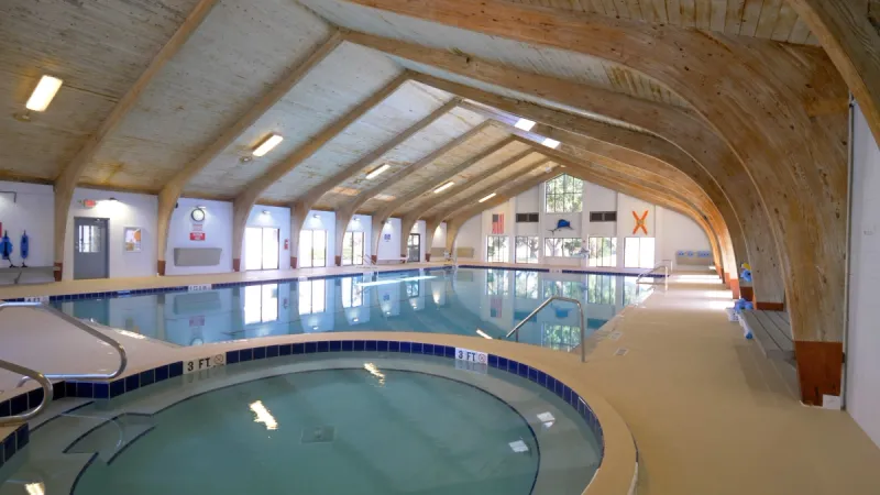 View of Scottish Highlands' indoor pool area with a hot tub in the foreground, plenty of tall windows and ample light shining through.