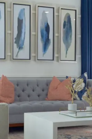 Grey couch with coral pillows, white coffee table, and framed photos of feathers on the wall.