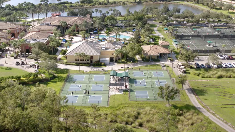 Aerial shot of Pelican Preserve's clubhouse and tennis courts amidst greenery.