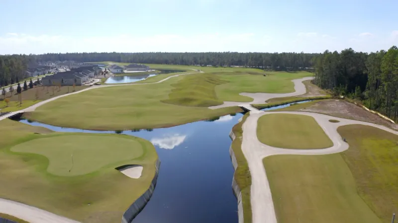 Aerial view of a golf course with multiple greens and sand traps, a winding blue water feature, and cart paths.