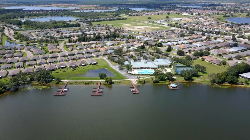 Aerial view of Traditions at Lake Ruby homes set upon a calm lake with boat docks and amenity center for residents to enjoy.