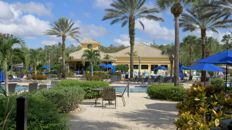 Pelican Preserve's vibrant poolside setting with blue umbrellas, palm trees, and a clubhouse.