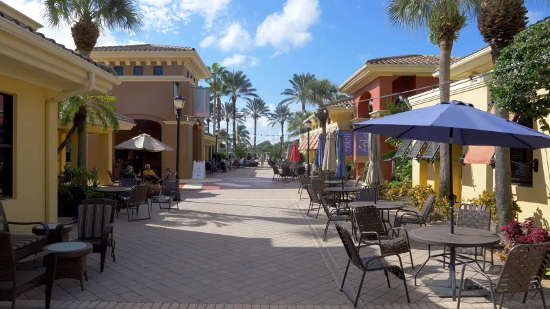 A bustling plaza with outdoor seating flanked by palm trees under sunny skies at Pelican Preserve.