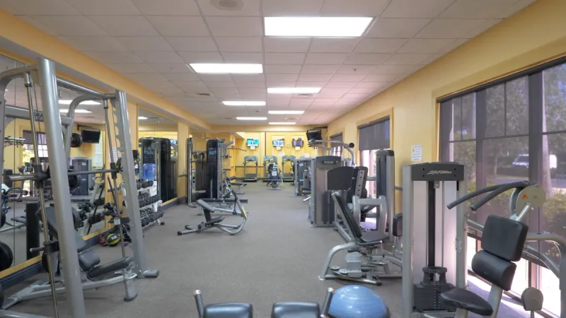 A fully equipped gym with vibrant yellow walls, featuring a variety of cardio equipment and TVs for entertainment, perfect for an energizing workout.