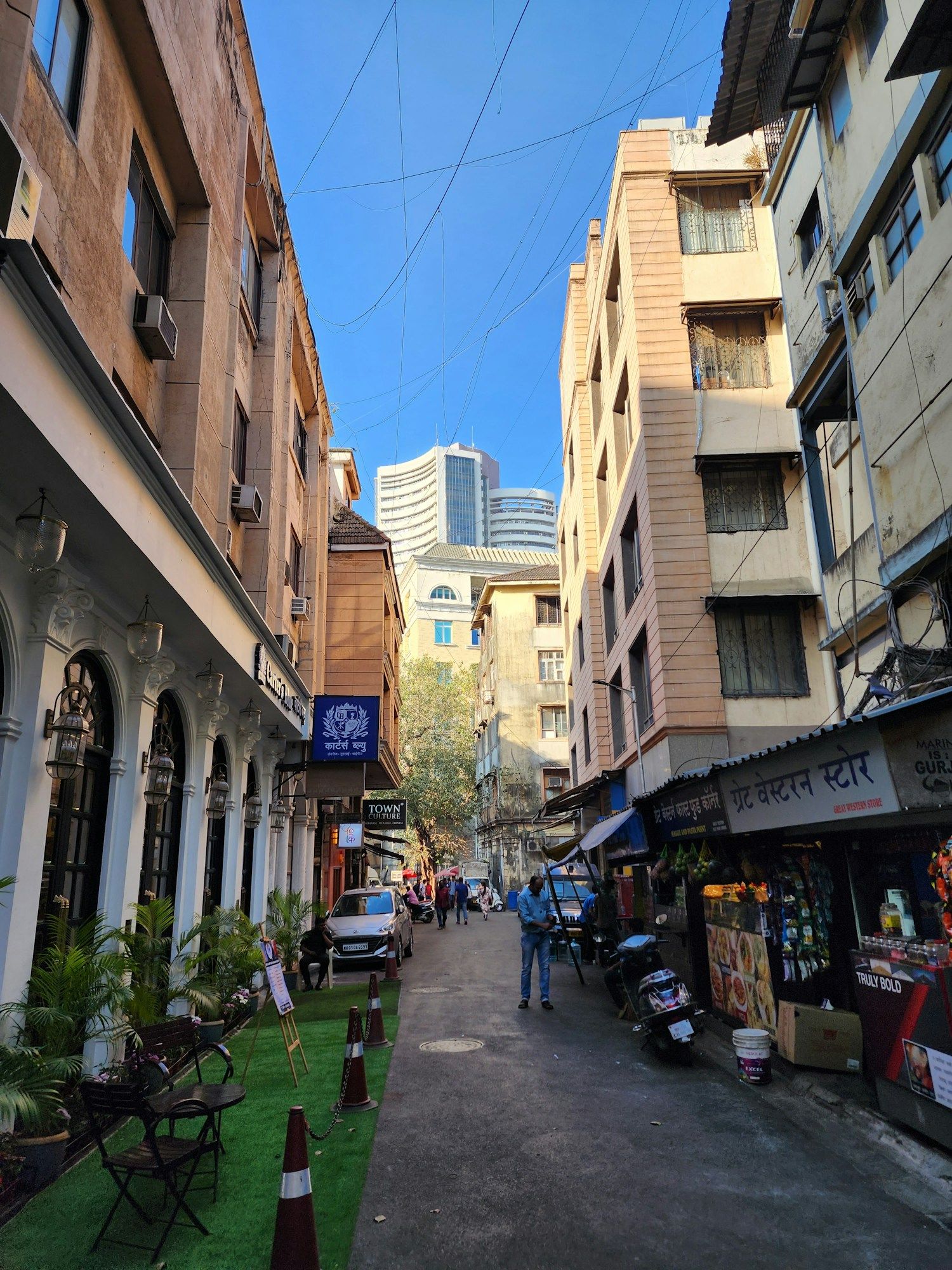 A narrow lane in Kala Ghoda in Mumbai, with an arcaded colonial building on the left, small shops on the right and office towers in the distance.