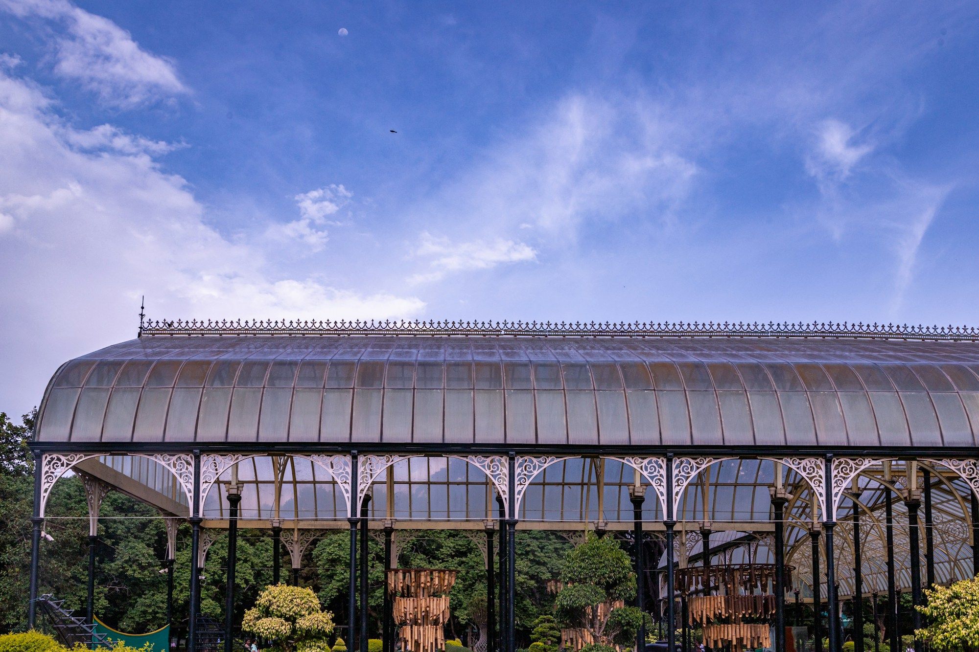 The iron-and-glass roof of the Glass House at Lalbagh Botanical Garden in Bengaluru, under a blue sky with thin clouds.