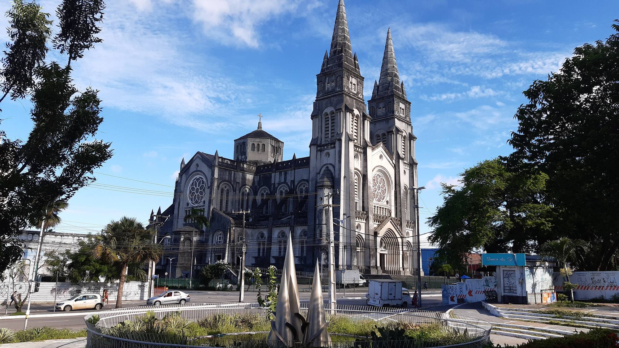 The twin spires of the Catedral Metropolitana in Fortaleza under a blue sky, with trees on either side and the plaza in front.