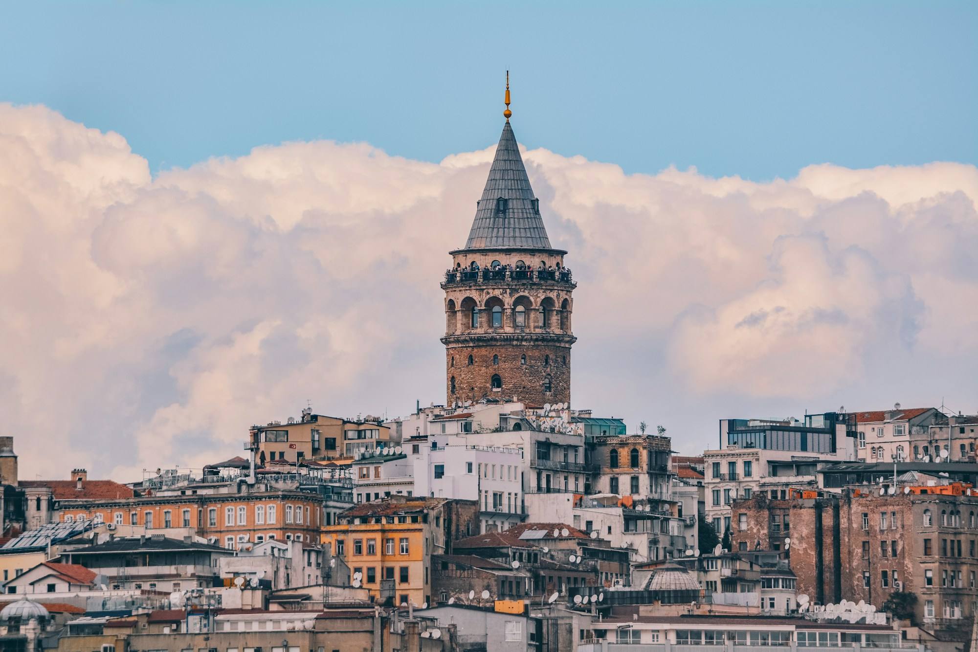 The Galata Tower rising above the rooftops of Beyoğlu in Istanbul, with white clouds behind it.