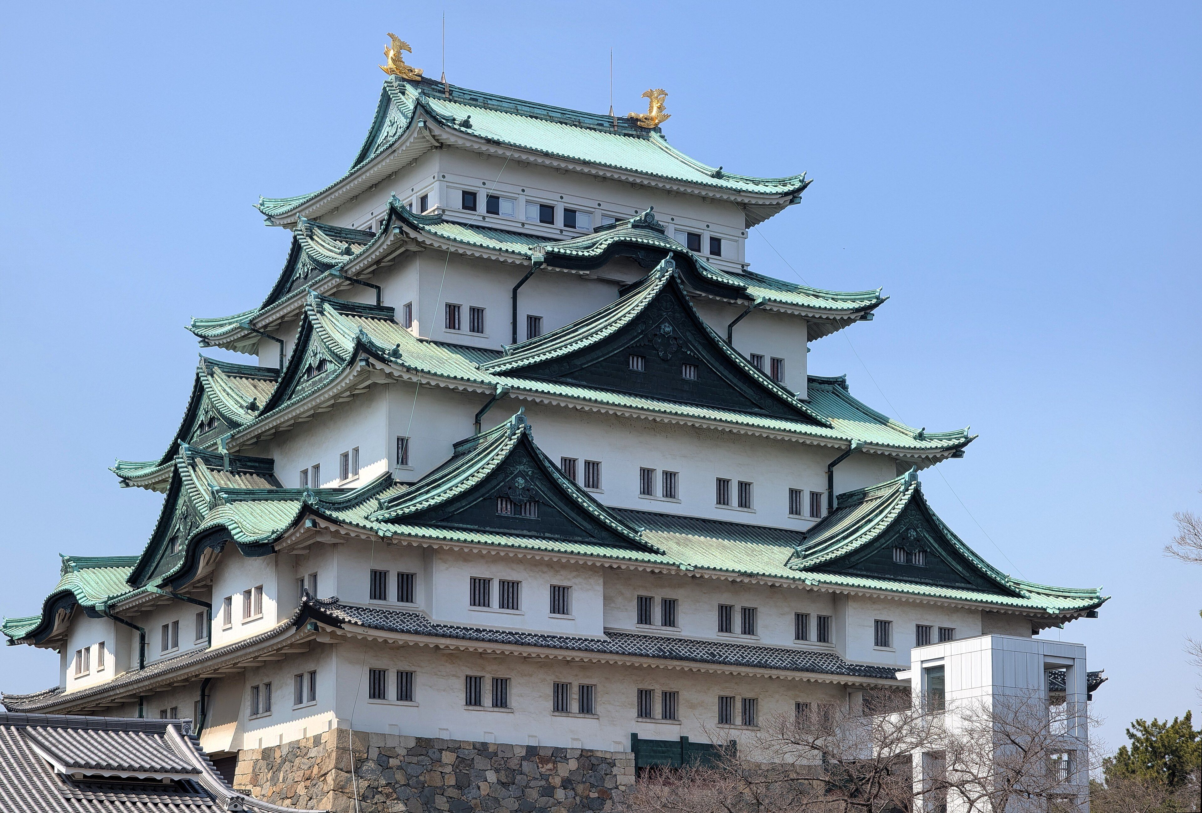 Nagoya Castle's keep with its green roofs and golden shachi ornaments under a blue sky.