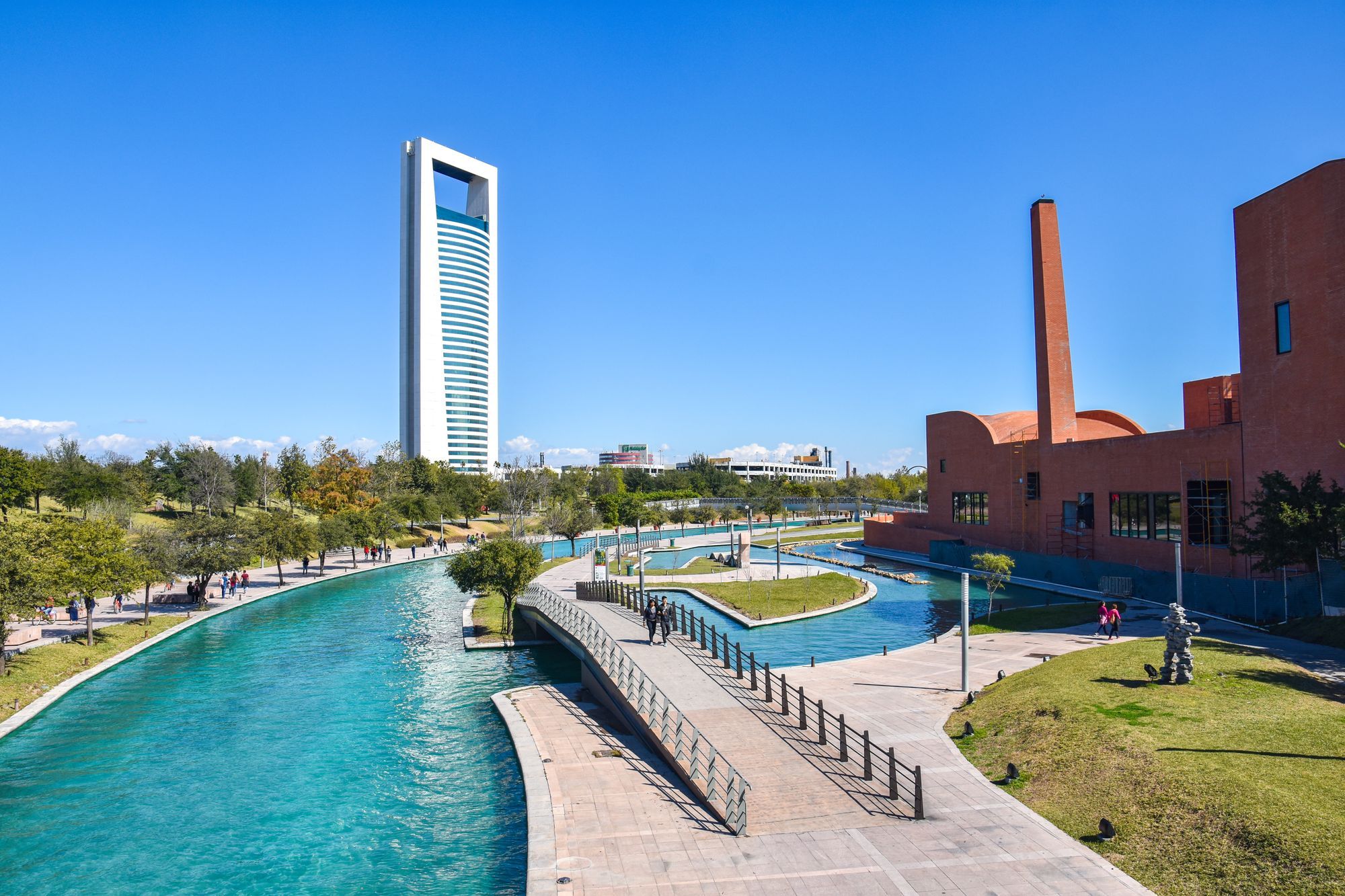 A canal in an urban park in Monterrey, with modern buildings and trees.