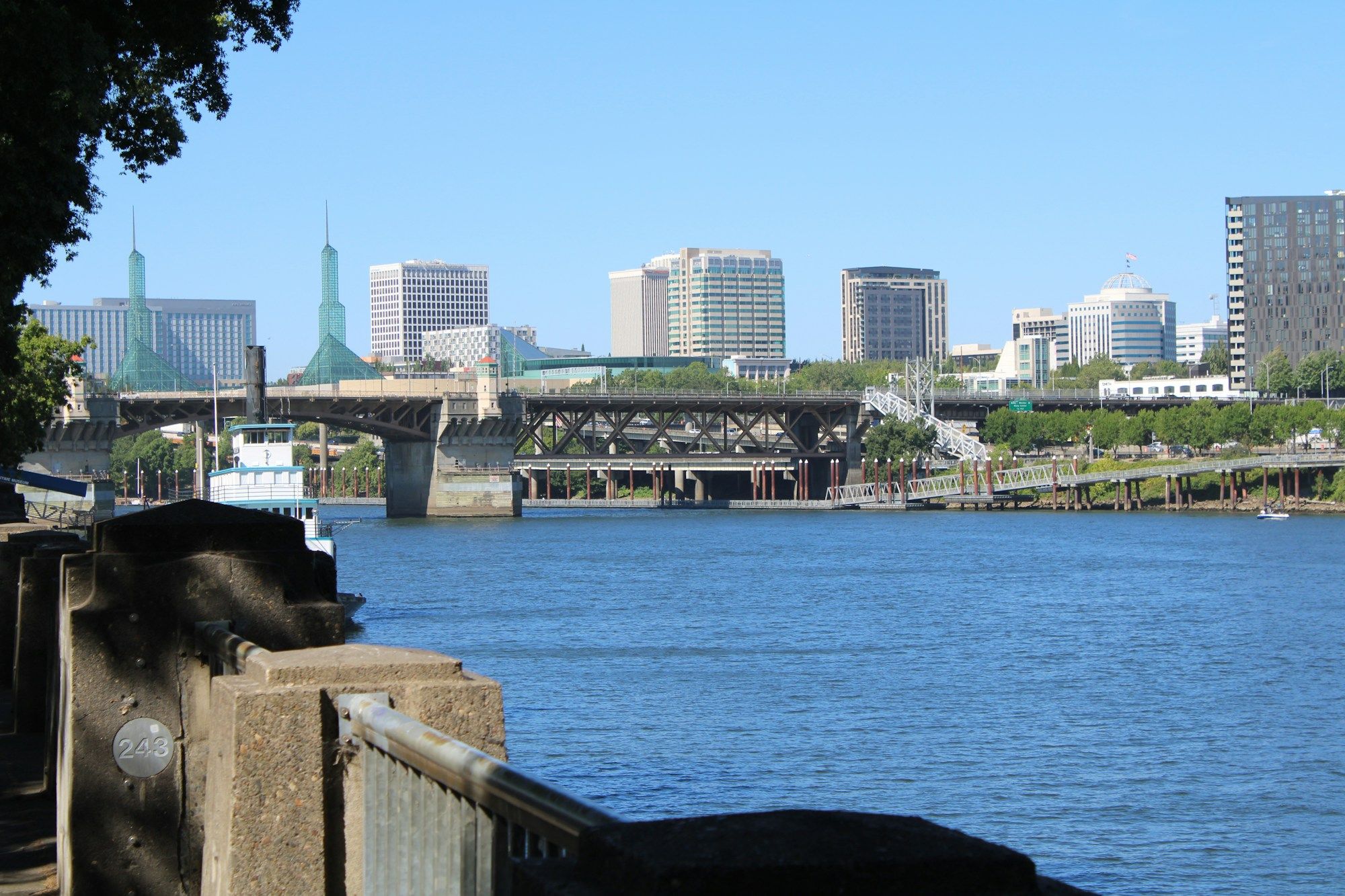 The downtown Portland skyline across the Willamette River, with a bridge and moored boats.