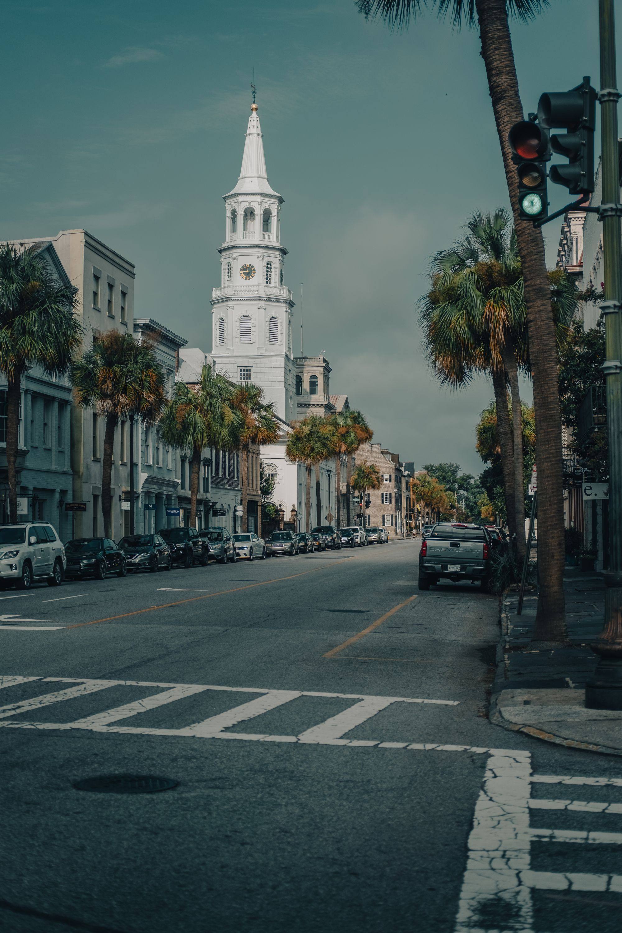 St. Michael's Church steeple above Meeting Street in Charleston, with palm trees and old townhouses.