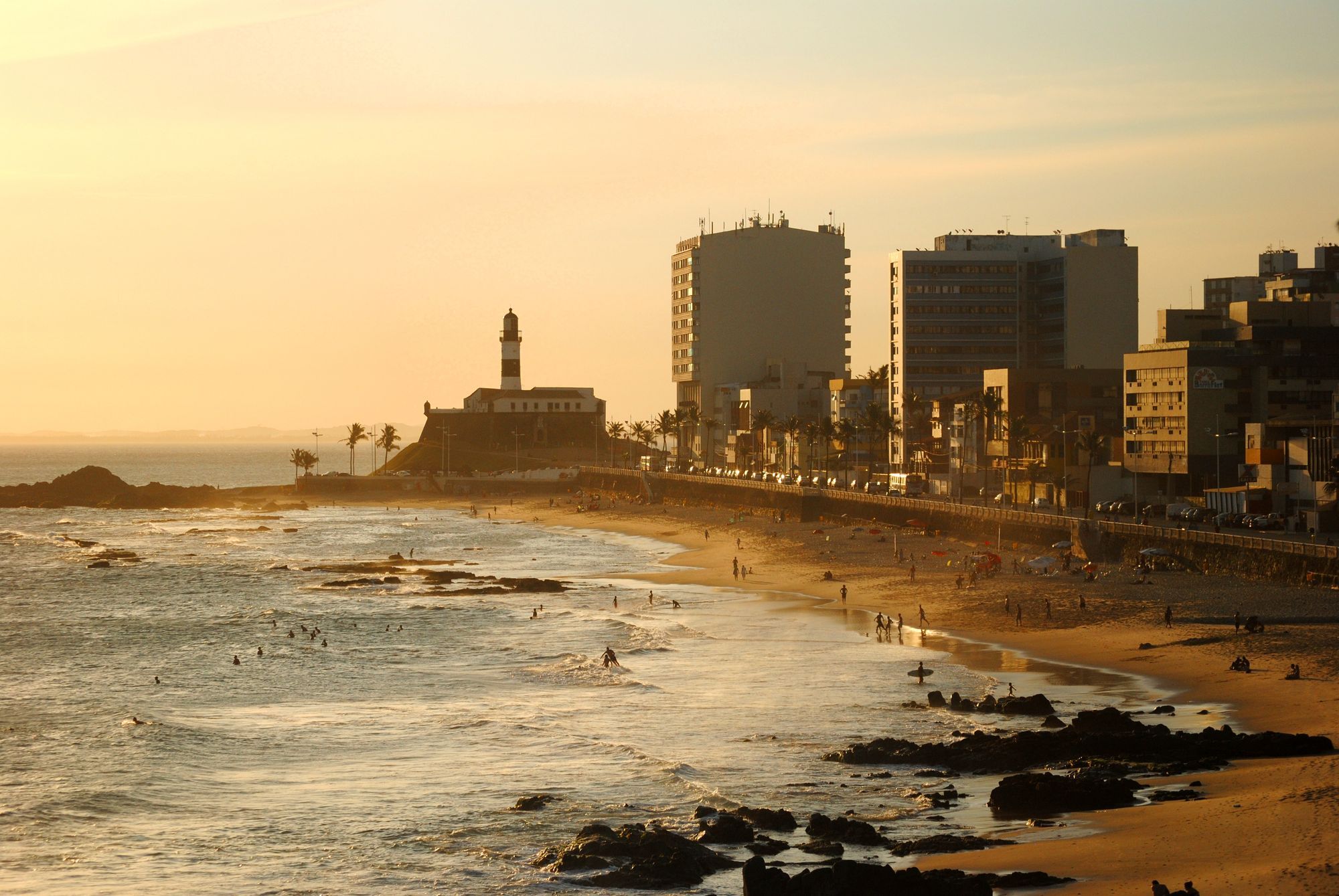 The Farol da Barra lighthouse and the Barra seafront in Salvador at sunset, with the beach in the foreground.