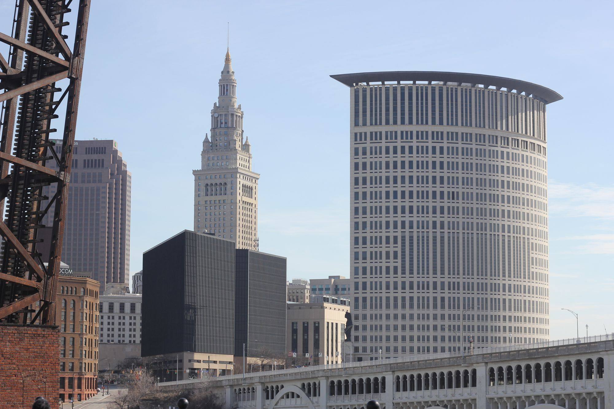 The Terminal Tower and other downtown Cleveland skyscrapers under a clear sky, with a rail bridge below.