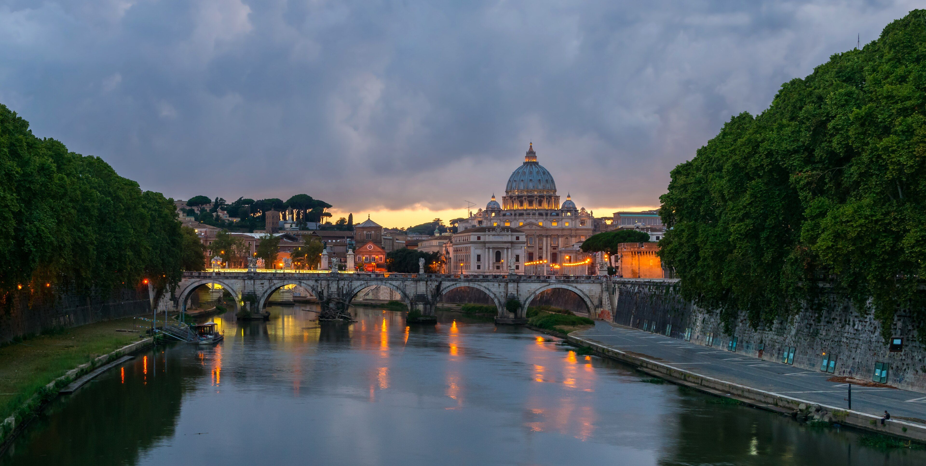 Ponte Sant'Angelo over the Tiber at dusk, with the dome of St Peter's behind it.