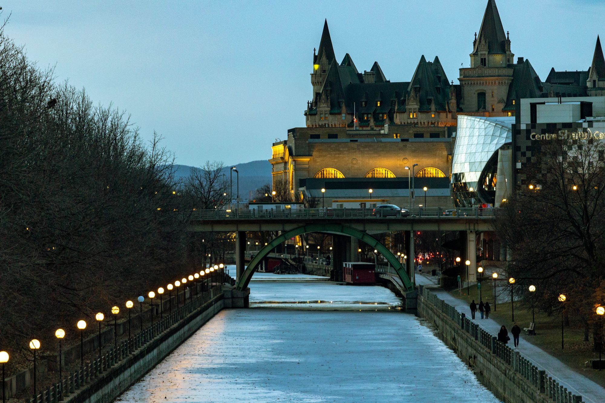 The Château Laurier above the frozen Rideau Canal in Ottawa at dusk, with lights along the skating path.